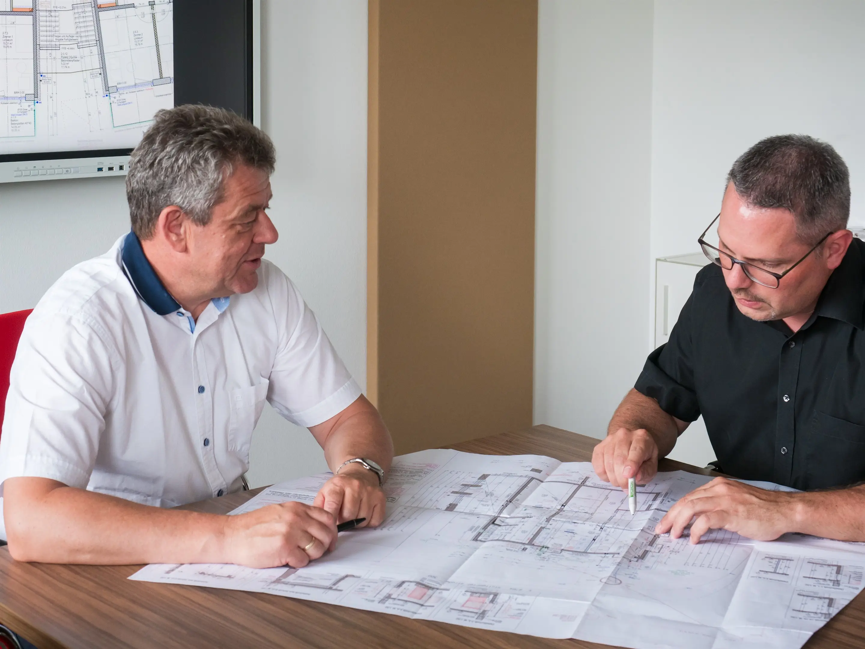 Zwei Planer arbeiten an einem Werkplan, einer zeigt mit dem Stift auf ein Detail